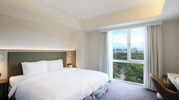 Une chambre d’hôtel avec un grand lit, un bureau et une vue sur le paysage urbain, visible à travers une grande fenêtre.