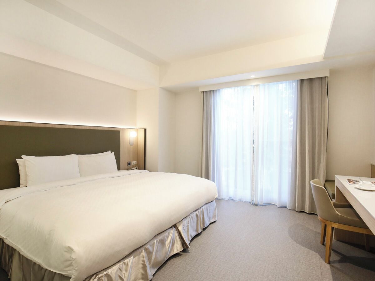A hotel room with a large bed, a desk, and a chair.