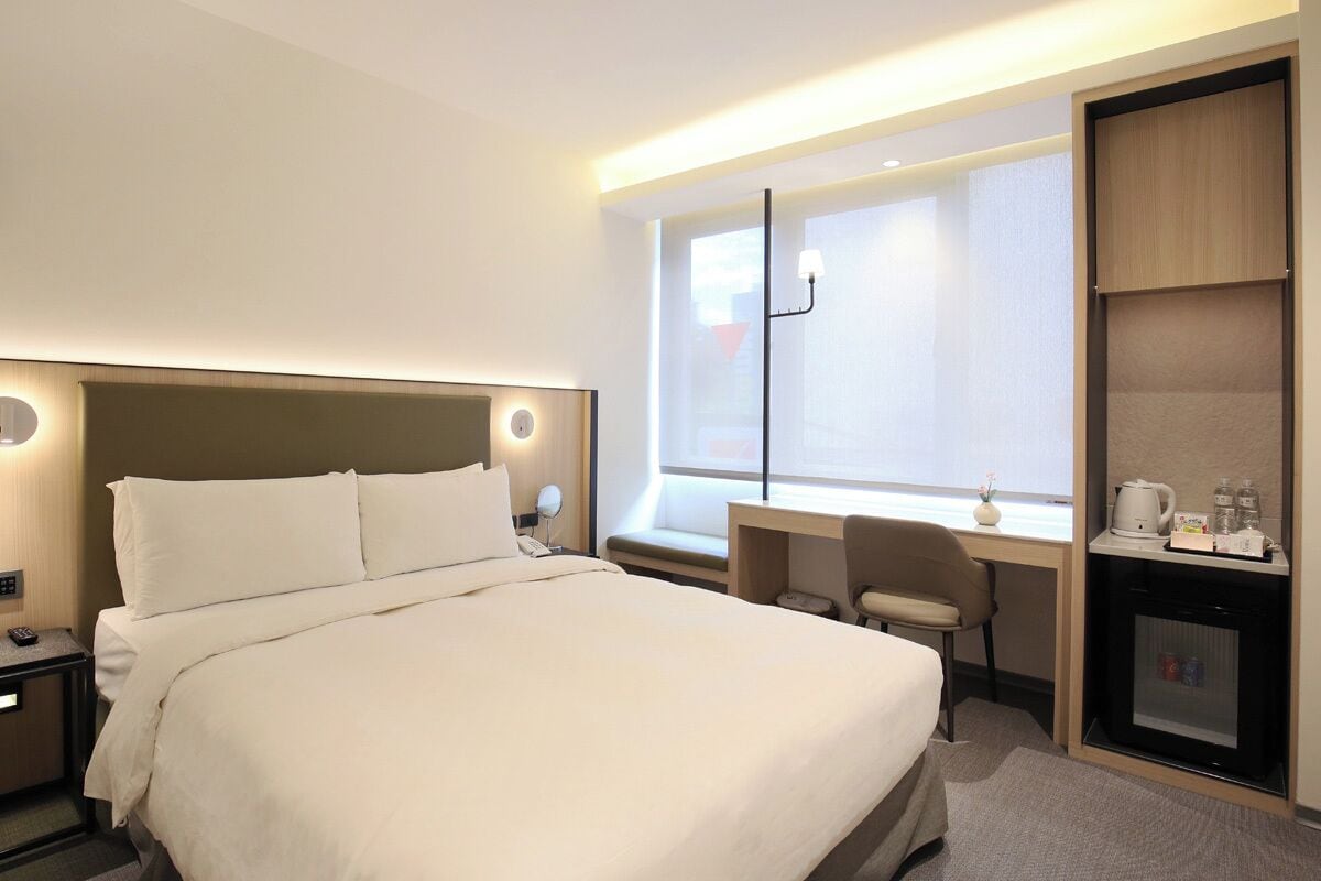 Una habitación de hotel con una cama grande, un escritorio con silla, un minibar y una ventana con persianas.