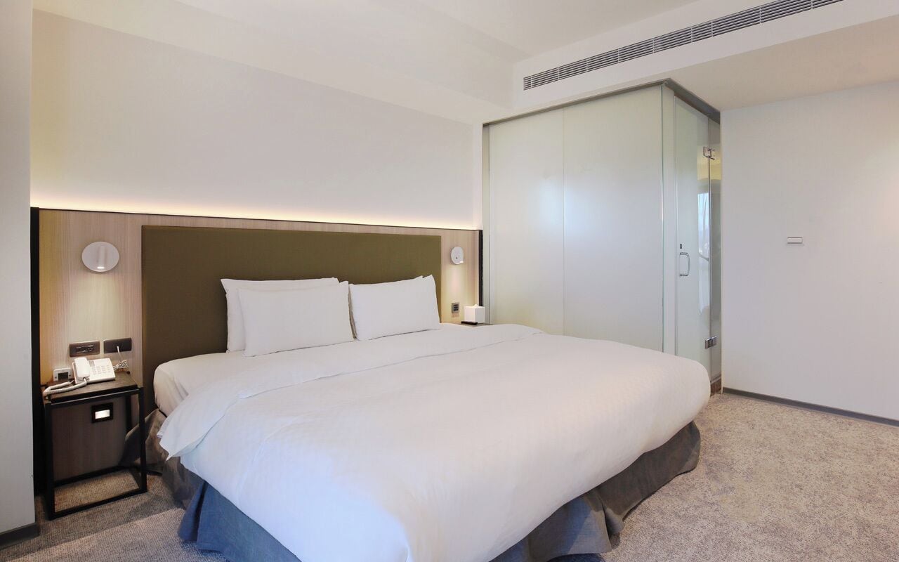 Ein Hotelzimmer mit einem großen Bett, Nachttischen, einer Ablagefläche und einer wandmontierten Lampe.