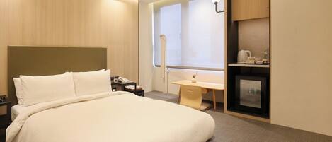 Una habitación de hotel con una cama grande, un escritorio, una kitchenette pequeña y una ventana con persianas.