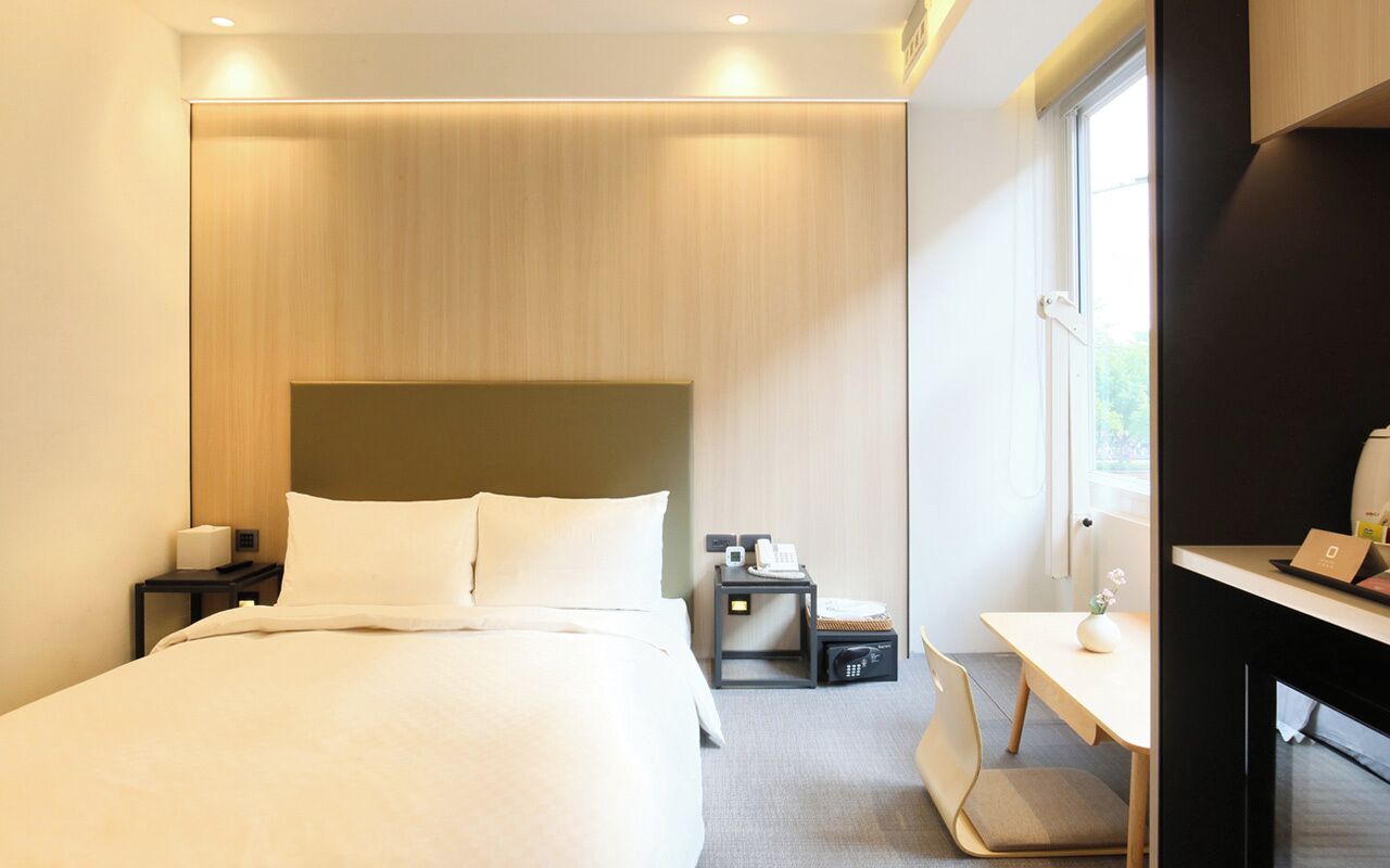 Una habitación de hotel moderna con una cama grande, mesitas de noche, un escritorio y una silla.