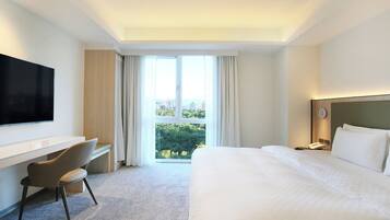 Habitación de hotel con cama, escritorio, silla, televisor y vista a la ciudad por la ventana.