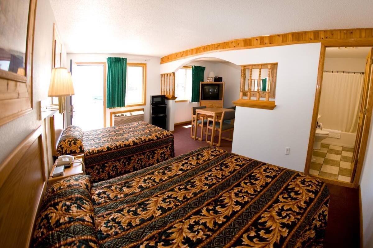 A hotel room with two beds, a desk, a television, and a bathroom.