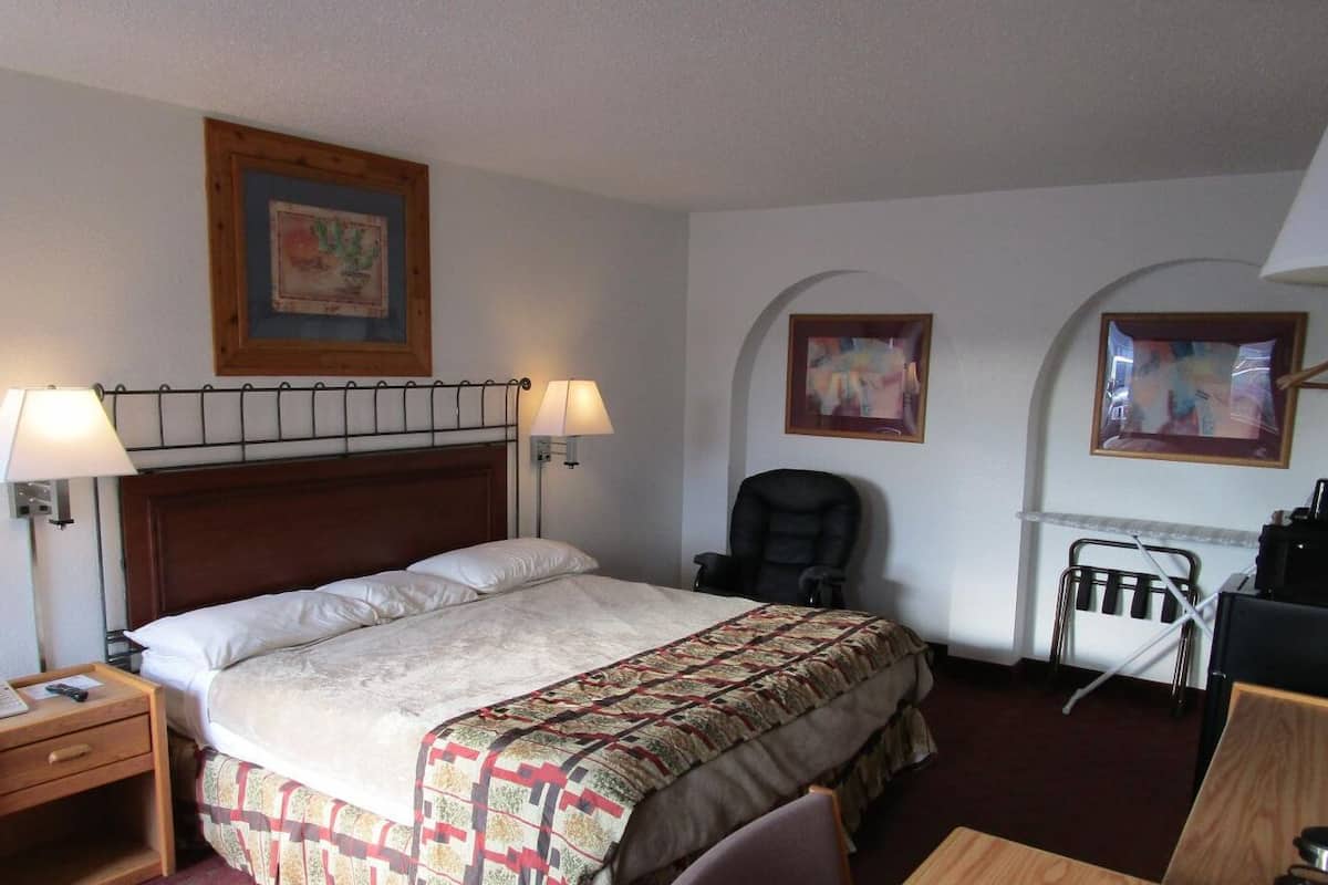 A hotel room with a bed, bedside lamps, a desk, and two chairs.