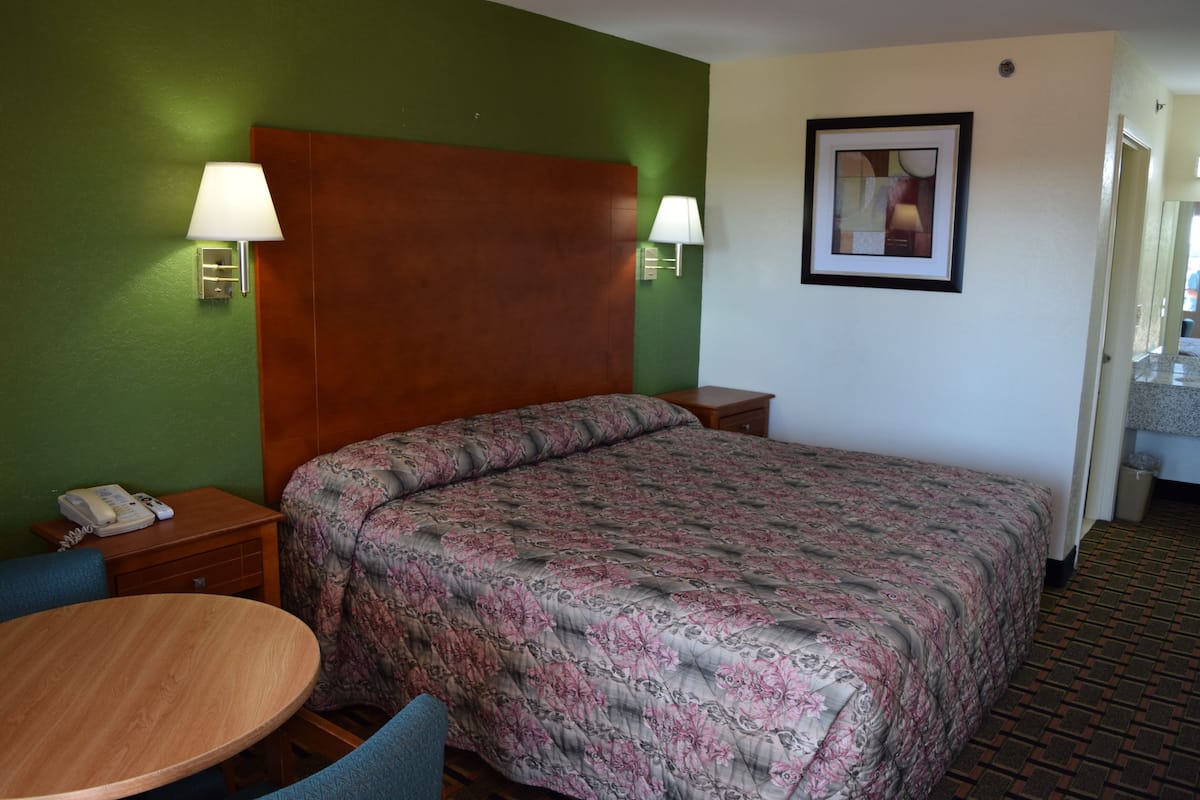 A hotel room with a large bed, two bedside lamps, a small table, and a chair.