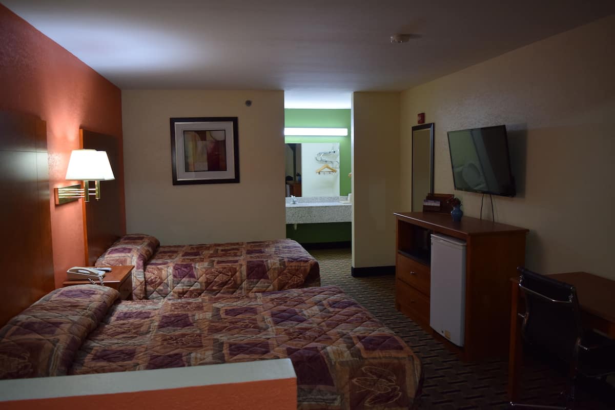 A hotel room with two beds, a desk, a television, and a small refrigerator.