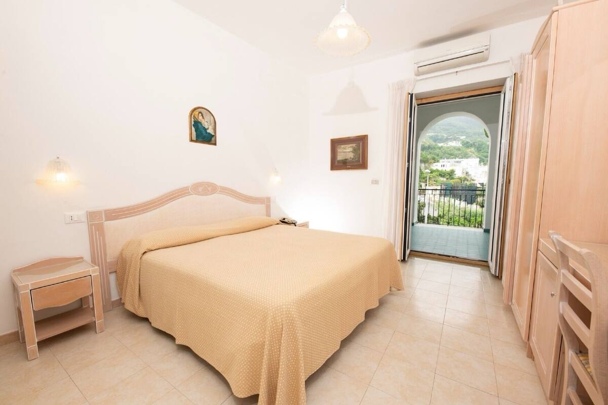 A bedroom with a bed, bedside table, wardrobe, and a view of a balcony.