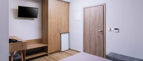 A modern bedroom with a bed, a desk, a wardrobe, a television, and a mini-fridge.