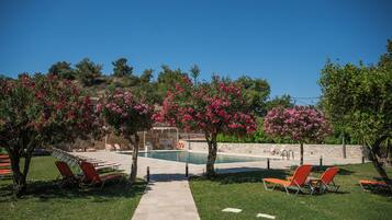 Un área de piscina con sillones de descanso, cielo despejado y árboles en flor.