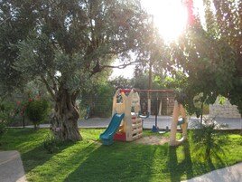 A playground with a slide and climbing structures, surrounded by trees and a fence.