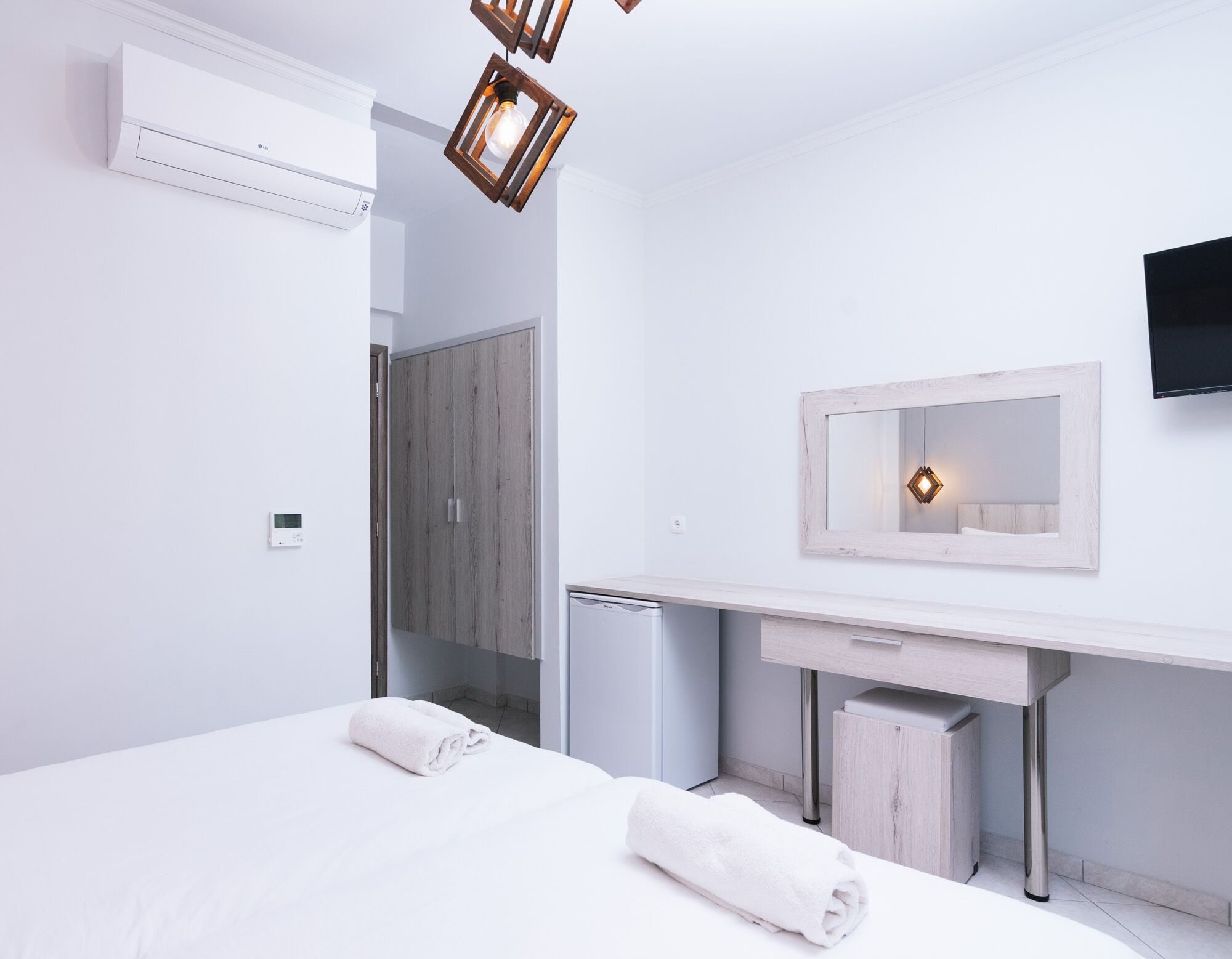 A modern hotel room with a bed, a small desk, a mirror, and a wall-mounted TV.