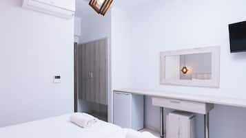 A modern hotel room with a bed, a small desk, a mirror, and a wall-mounted TV.