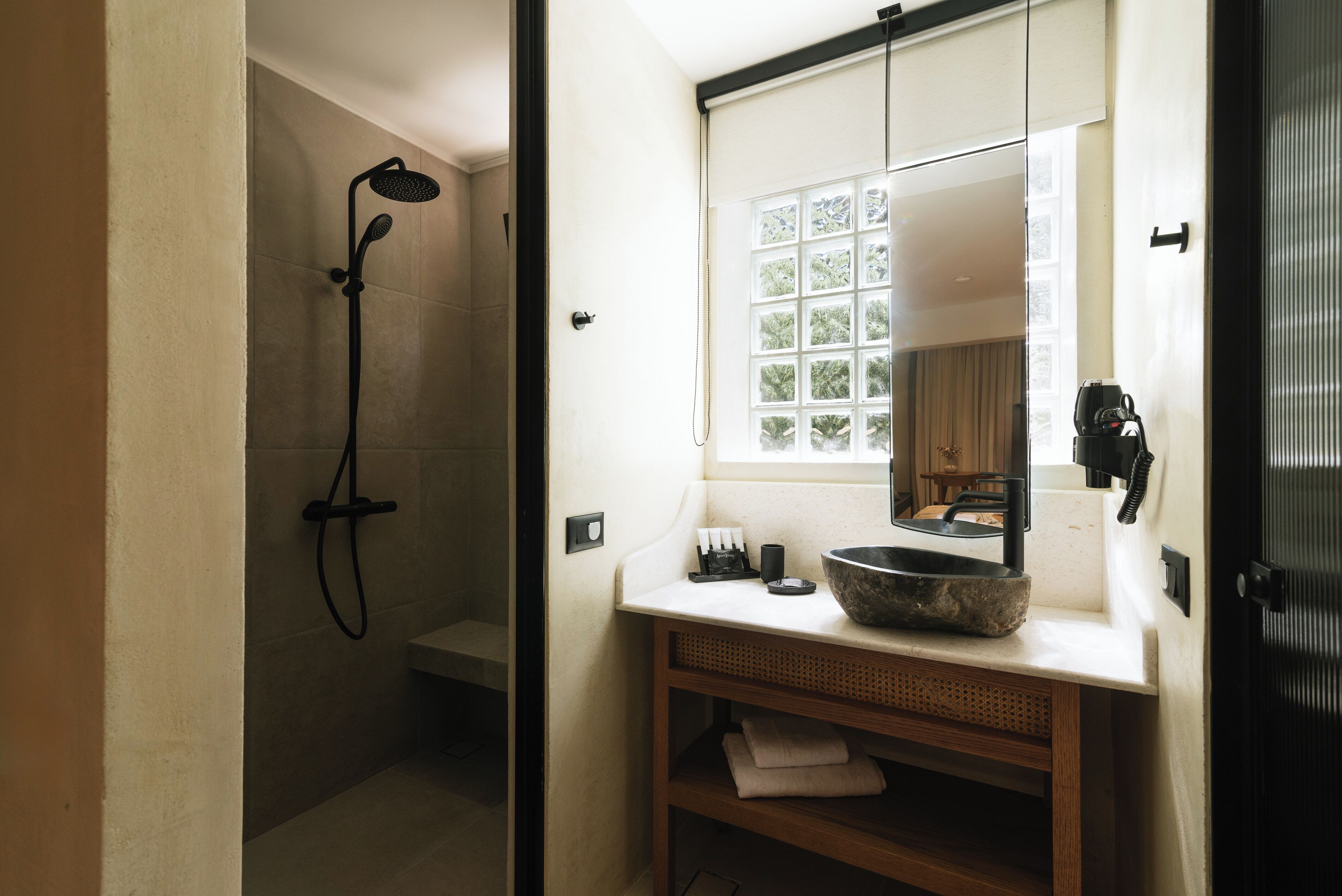 A bathroom with a shower, a sink with a large basin, and a window with a view of trees.