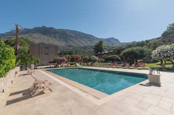 Une piscine avec une vue sur les montagnes, des espaces de détente en plein air et un mur en pierre.