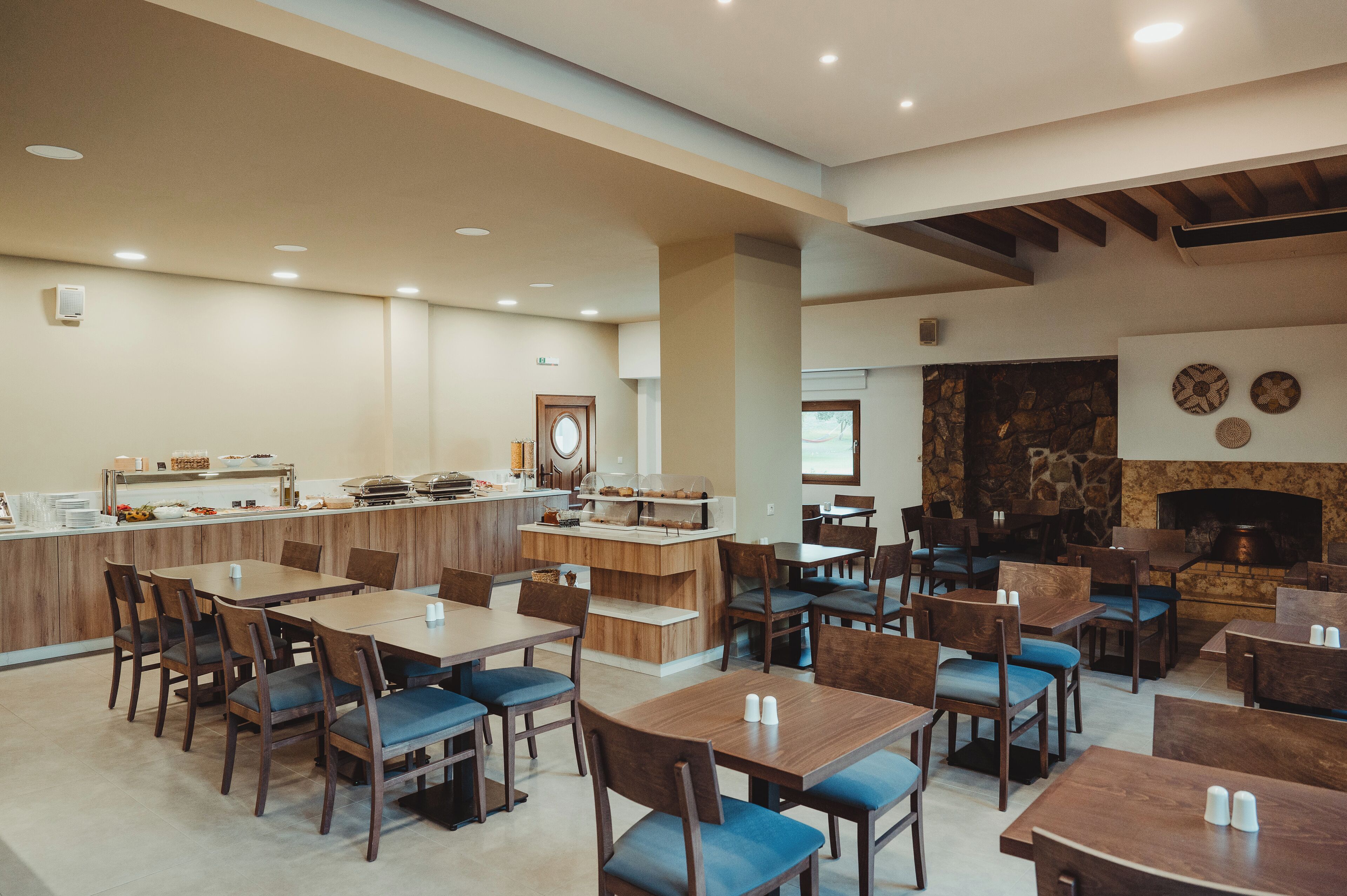 A spacious dining area with multiple tables and chairs, a kitchen counter, and a stone fireplace.