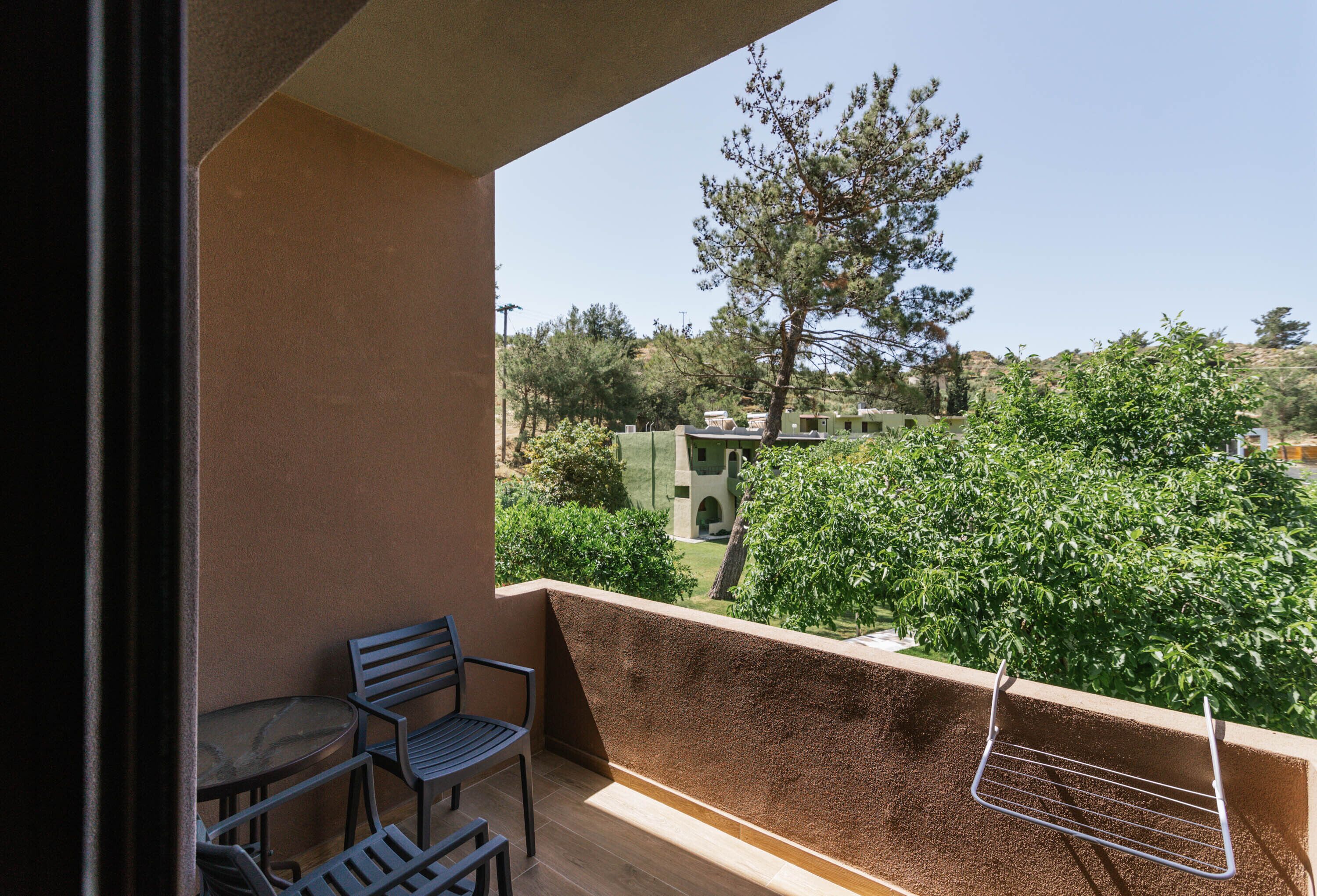 En balkon med et bord og stole, en tøjstativ og udsigt over et grønt landskab med træer og bygninger.