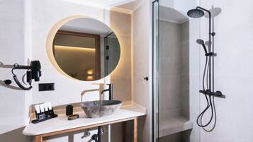 A modern bathroom with a round mirror, a sink with a stone basin, and a glass-enclosed shower area.