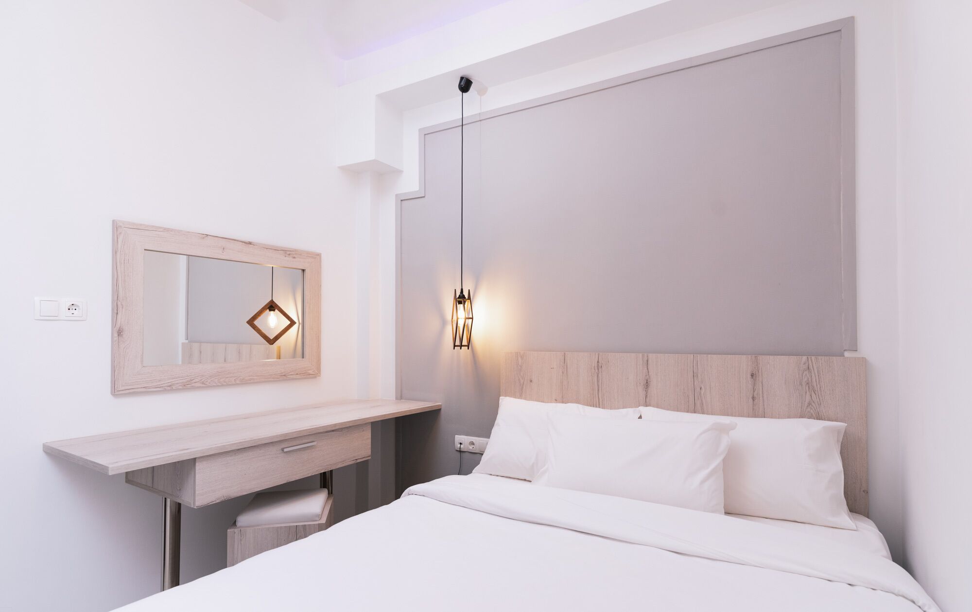 A modern bedroom with a wooden headboard, a bedside table with a mirror, and a wall-mounted light fixture.