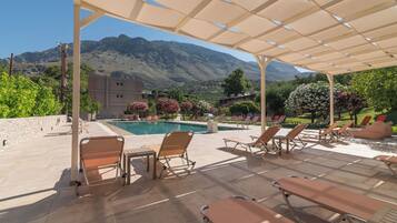 A poolside area with lounge chairs, a pergola, and a mountain view.