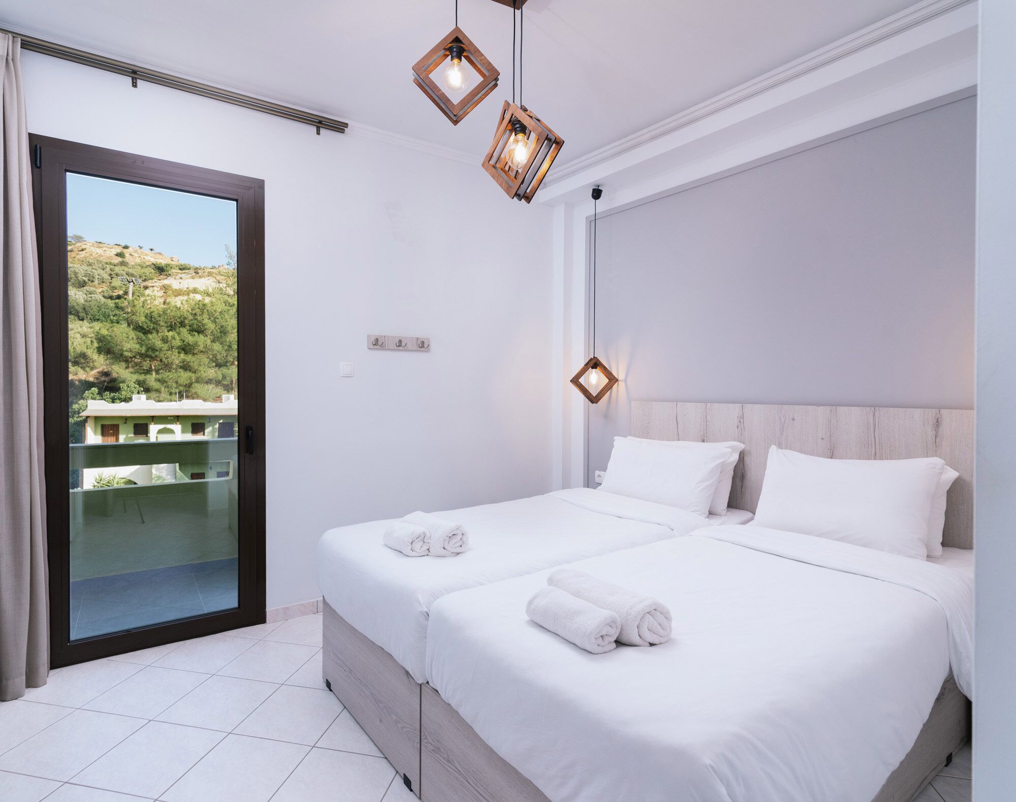 A hotel room with a balcony, a bed with white linens, and two pendant lights.