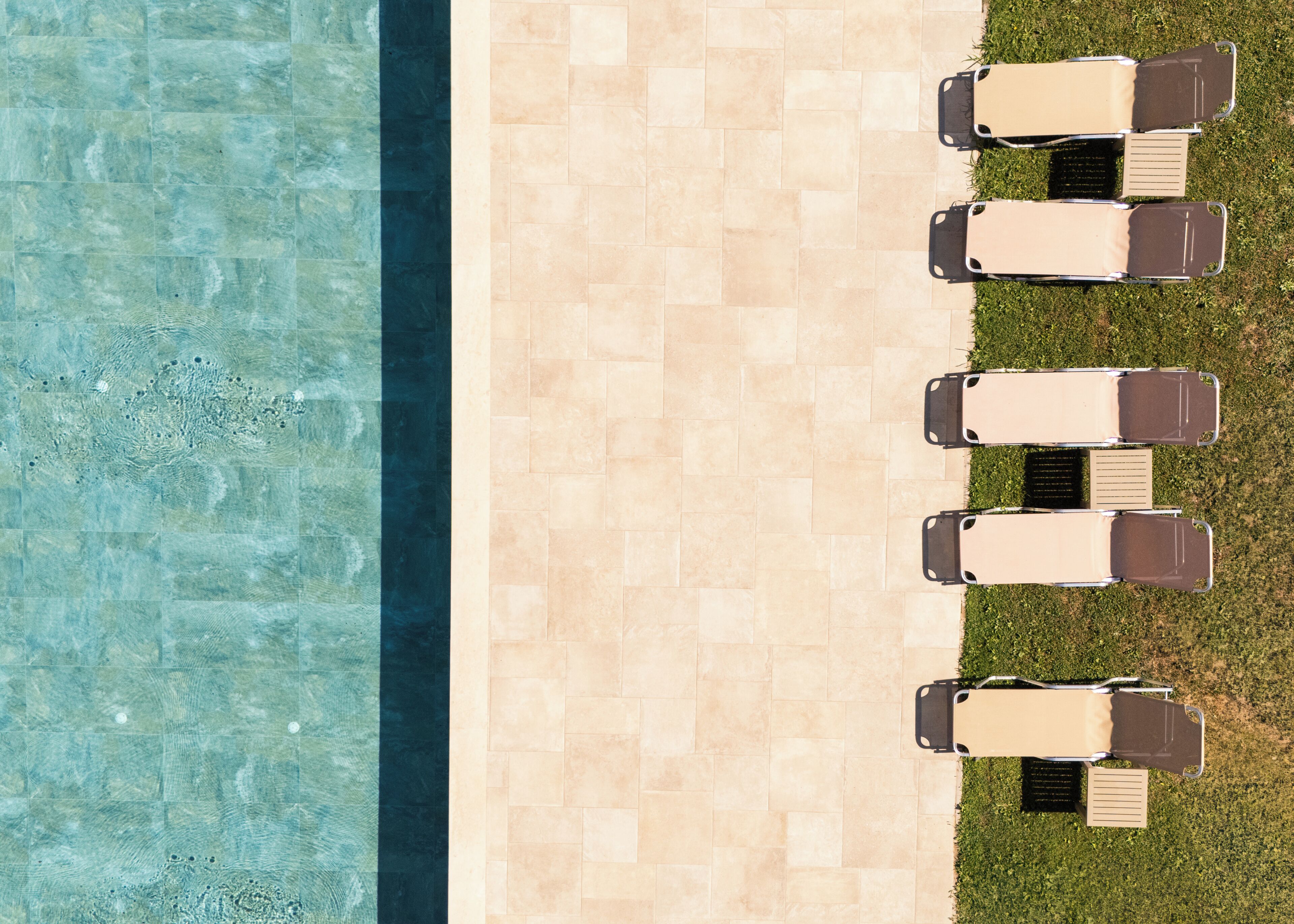 An aerial view of a pool area with a tiled walkway and four lounge chairs aligned on one side.