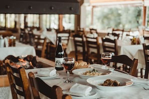 A restaurant interior with wooden chairs, white tablecloths, and a bottle of wine on the table.