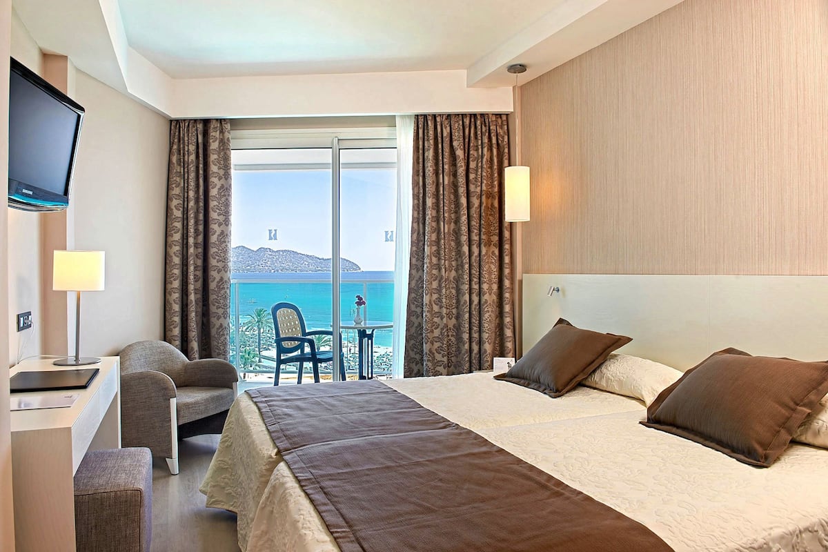 Ein Hotelzimmer mit Bett, Schreibtisch, Stuhl, Fernseher und Meerblick.