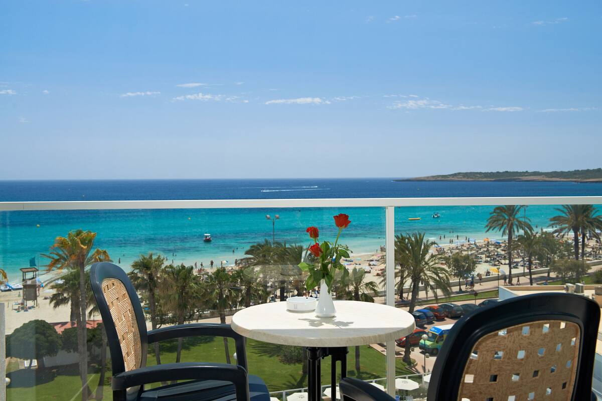 Ein Balkon mit Tisch und Stühlen mit Blick auf einen Strand, an dem Palmen und das Meer zu sehen sind.