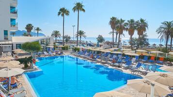 Relax by the pool surrounded by palm trees and lounge chairs, with the ocean visible in the distance.