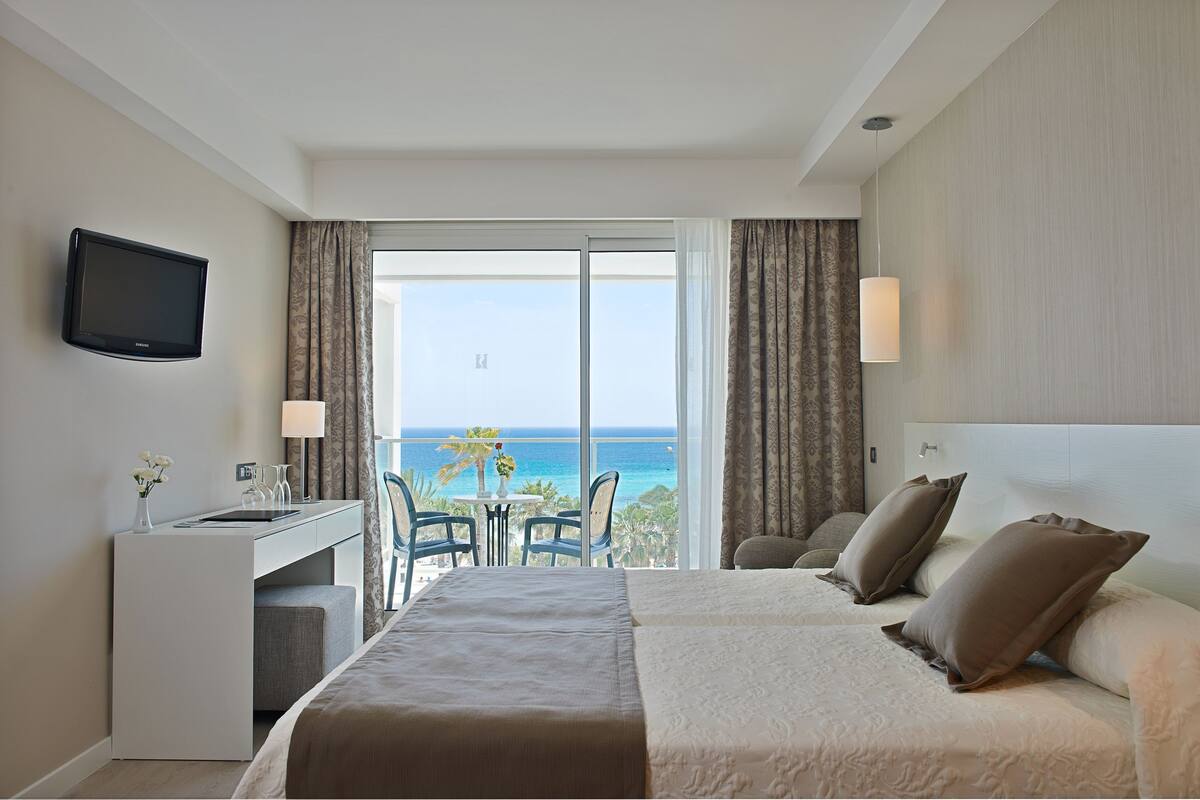 Ein Hotelzimmer mit Bett, Schreibtisch und Blick auf den Ozean.
