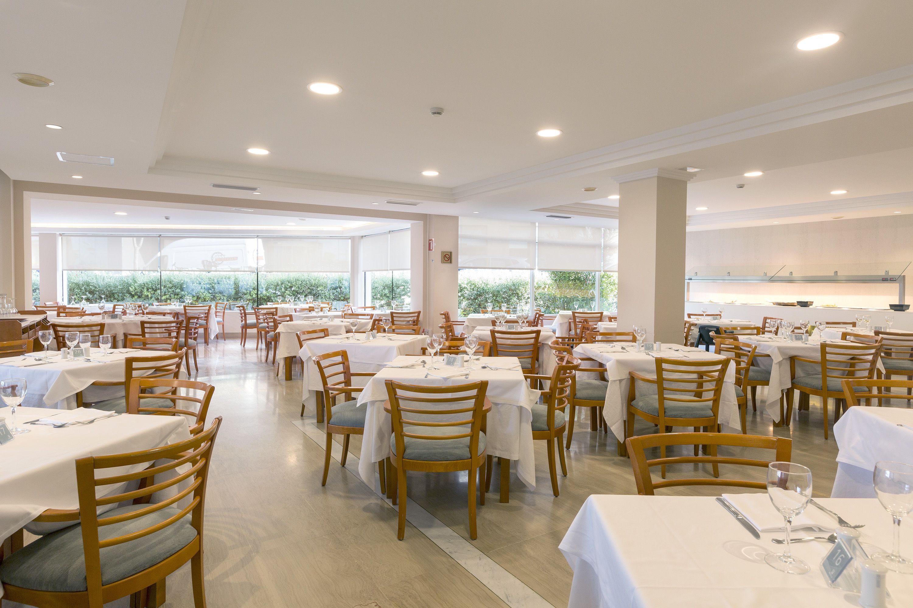 Un vaste espace dédié à la salle à manger, avec de nombreuses tables et chaises, et de grandes fenêtres donnant sur un paysage verdoyant.