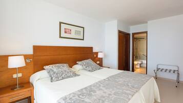 Un dormitorio ordenado con una cama, mesitas de noche, un cuadro enmarcado y un baño visible a través de una puerta abierta.