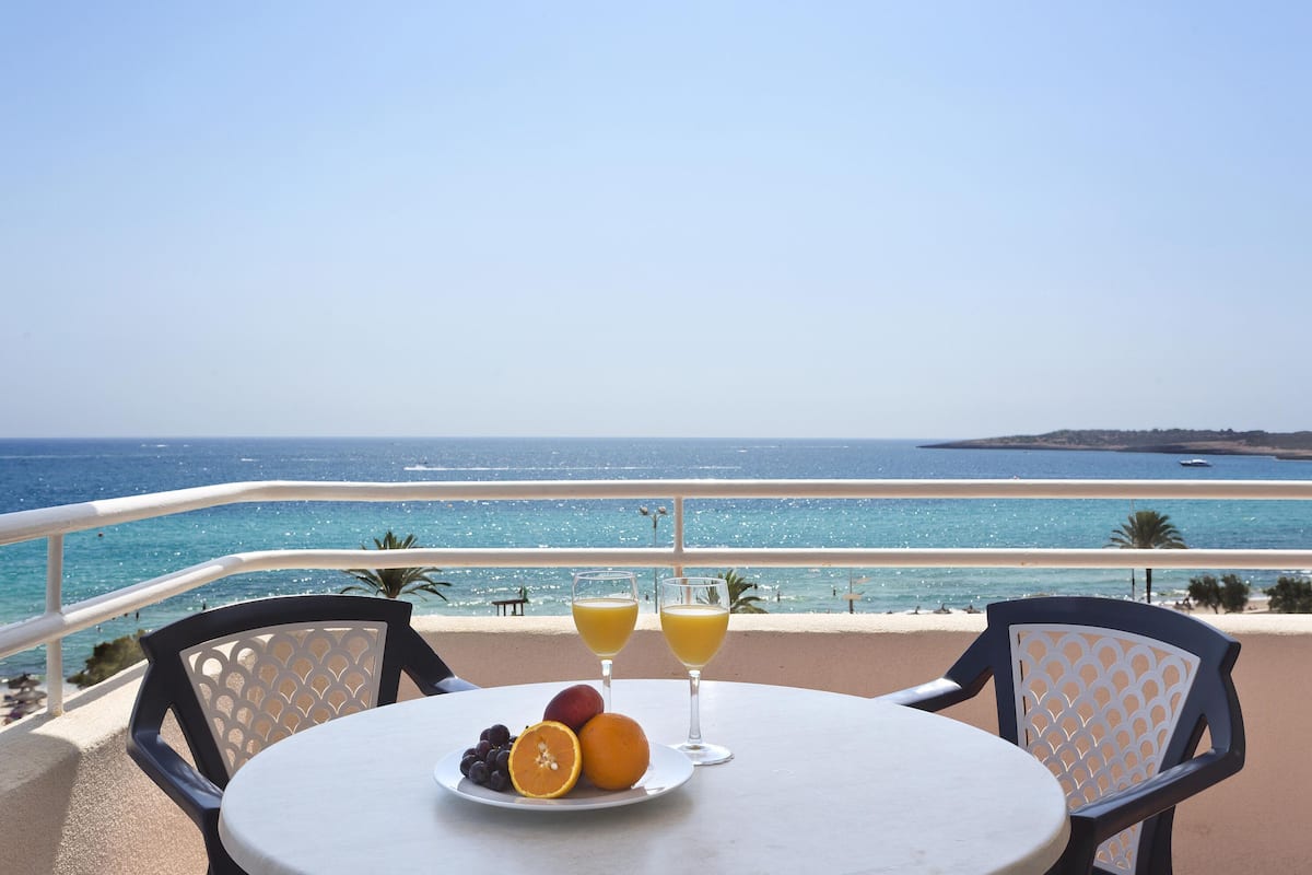 Una mesa con un plato de fruta y dos vasos de jugo de naranja, con vista a una playa y una vista despejada del mar y una isla distante.
