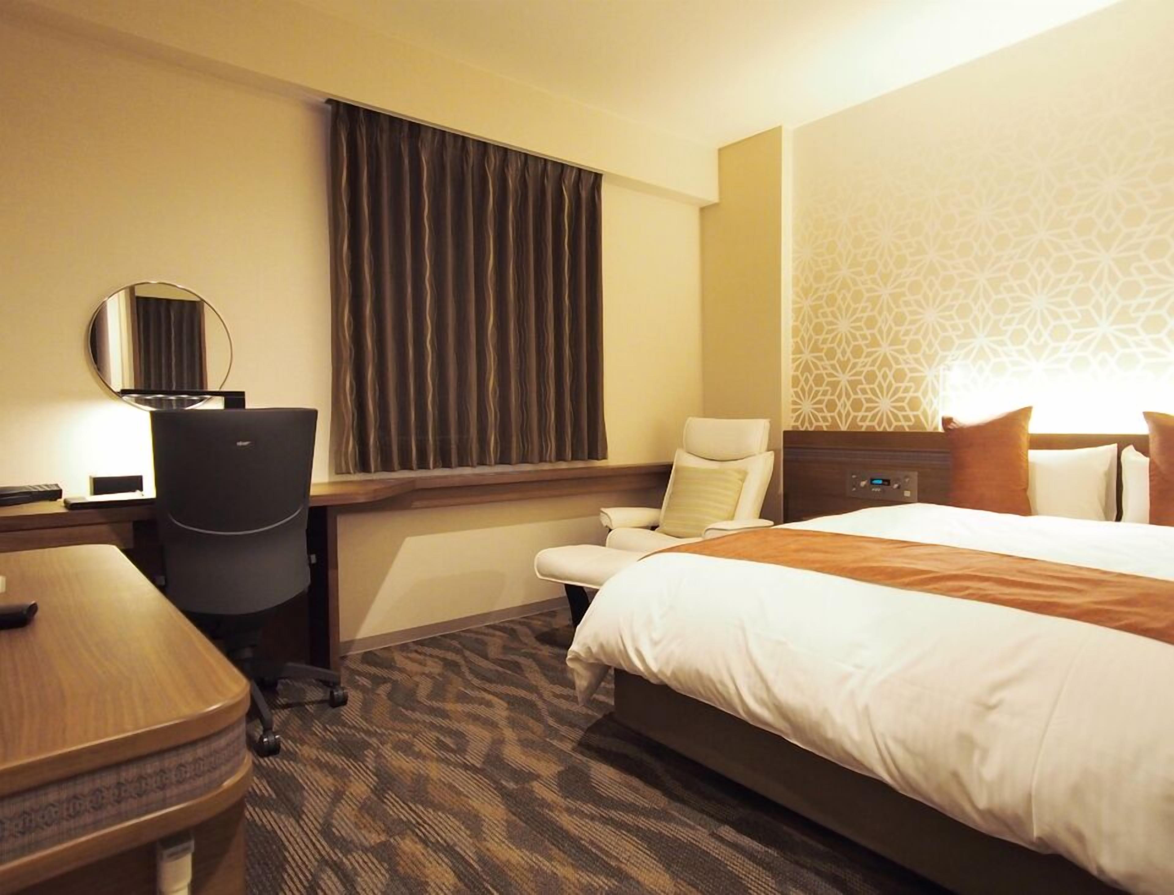 Ein Hotelzimmer mit Bett, Schreibtisch, Stuhl und einem großen Fenster mit Vorhängen.