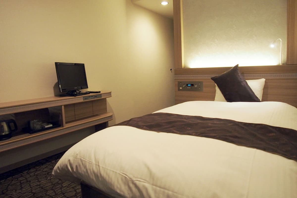 A hotel room with a bed, a television on a wooden stand, and a control panel on the wall.
