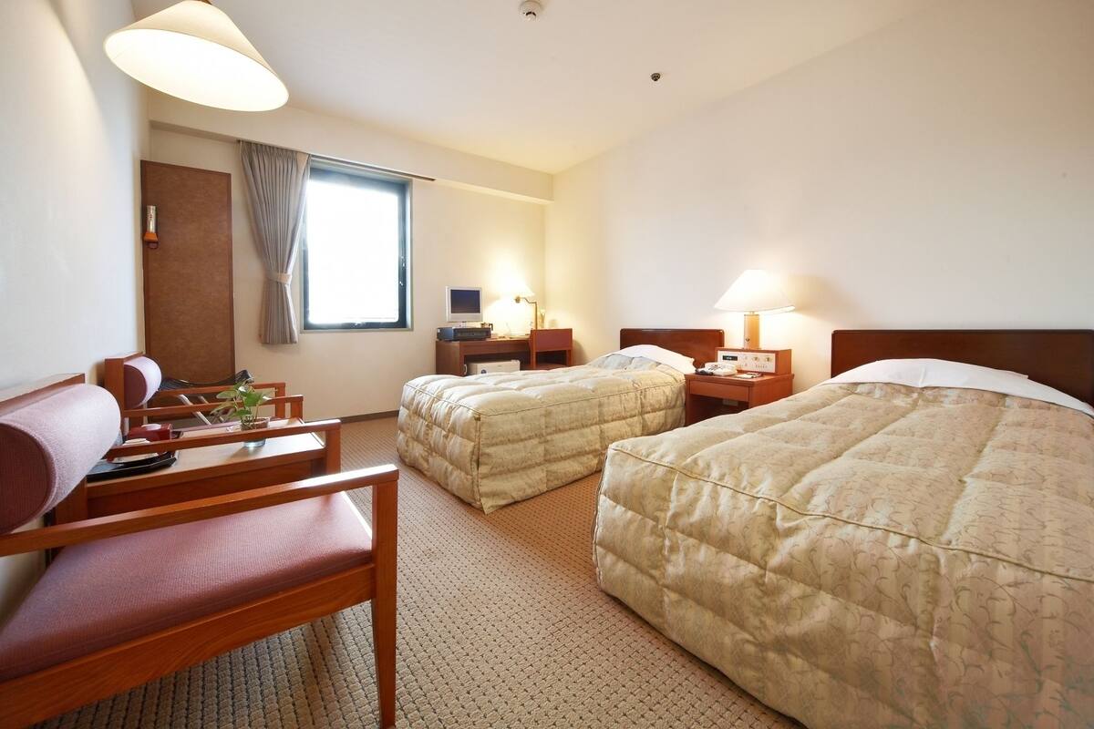 A hotel room with two beds, a desk, a chair, a TV, and a window with curtains.