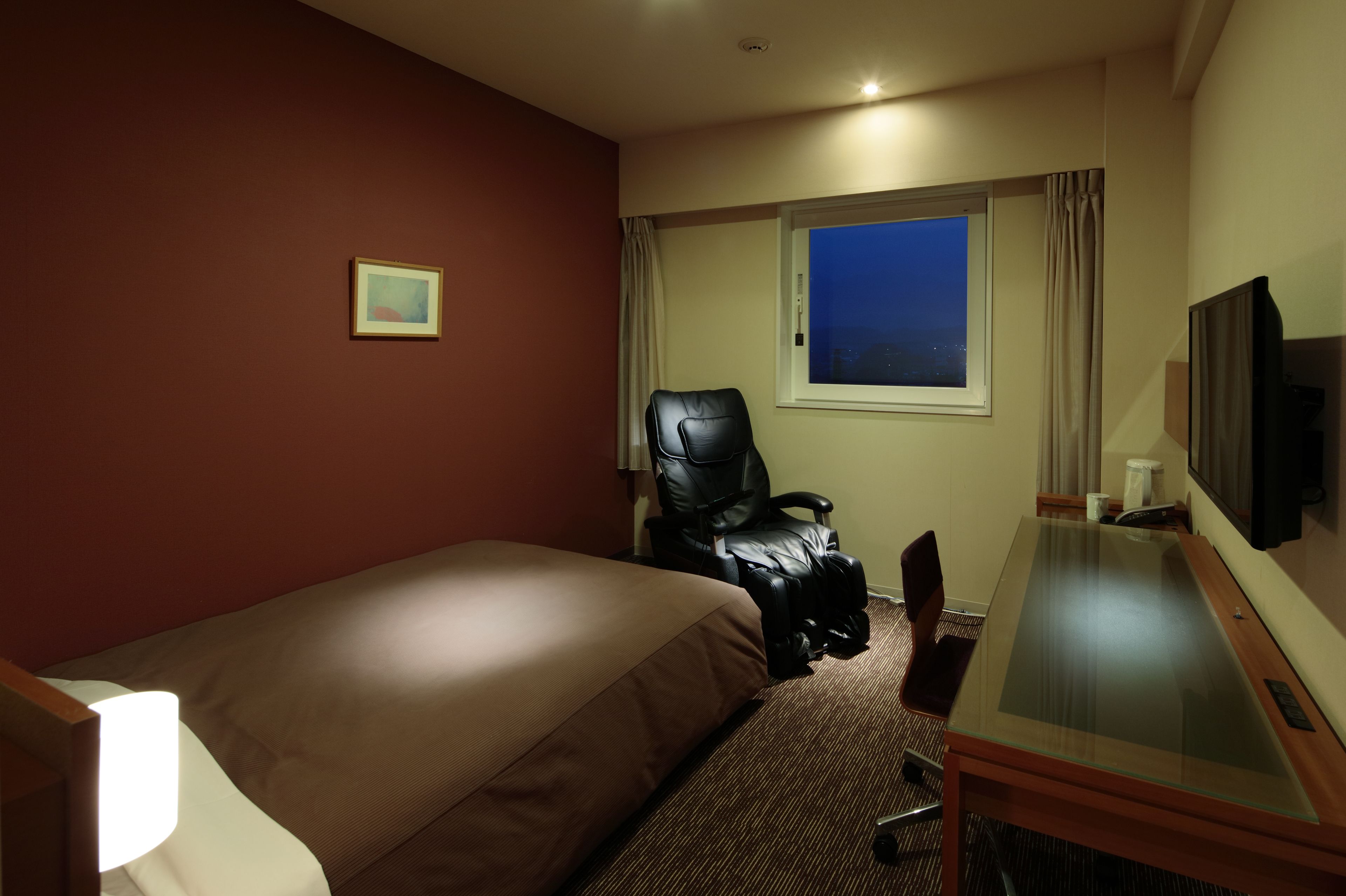 Ett hotellrum med en säng, ett skrivbord, en stol, en tv och ett fönster med gardiner.