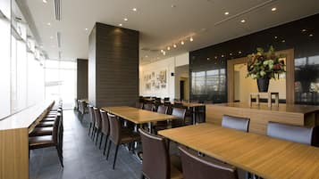 Un espace de restauration moderne, doté de longues tables et de chaises, d’une grande fenêtre et d’un mur orné de tableaux encadrés.