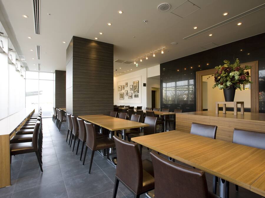 Un espace de restauration moderne, doté de longues tables et de chaises, d’une grande fenêtre et d’un mur orné de tableaux encadrés.