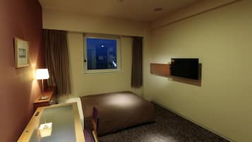 A hotel room with a bed, a desk, a television, a window with a city view, and a night sky visible through the window.