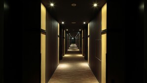 A long, narrow hallway with wooden flooring and walls, illuminated by overhead lights. - Candeo Hotels Kameyama (Kameyama)