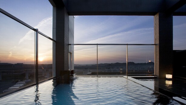An infinity pool with a clear view of the sunset over the cityscape. - Candeo Hotels Kameyama (Kameyama)