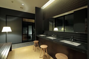 Un baño moderno con tres lavamanos, un espejo grande y taburetes de madera.