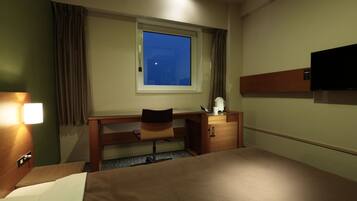 A hotel room with a bed, a desk, a chair, a window, and a television.
