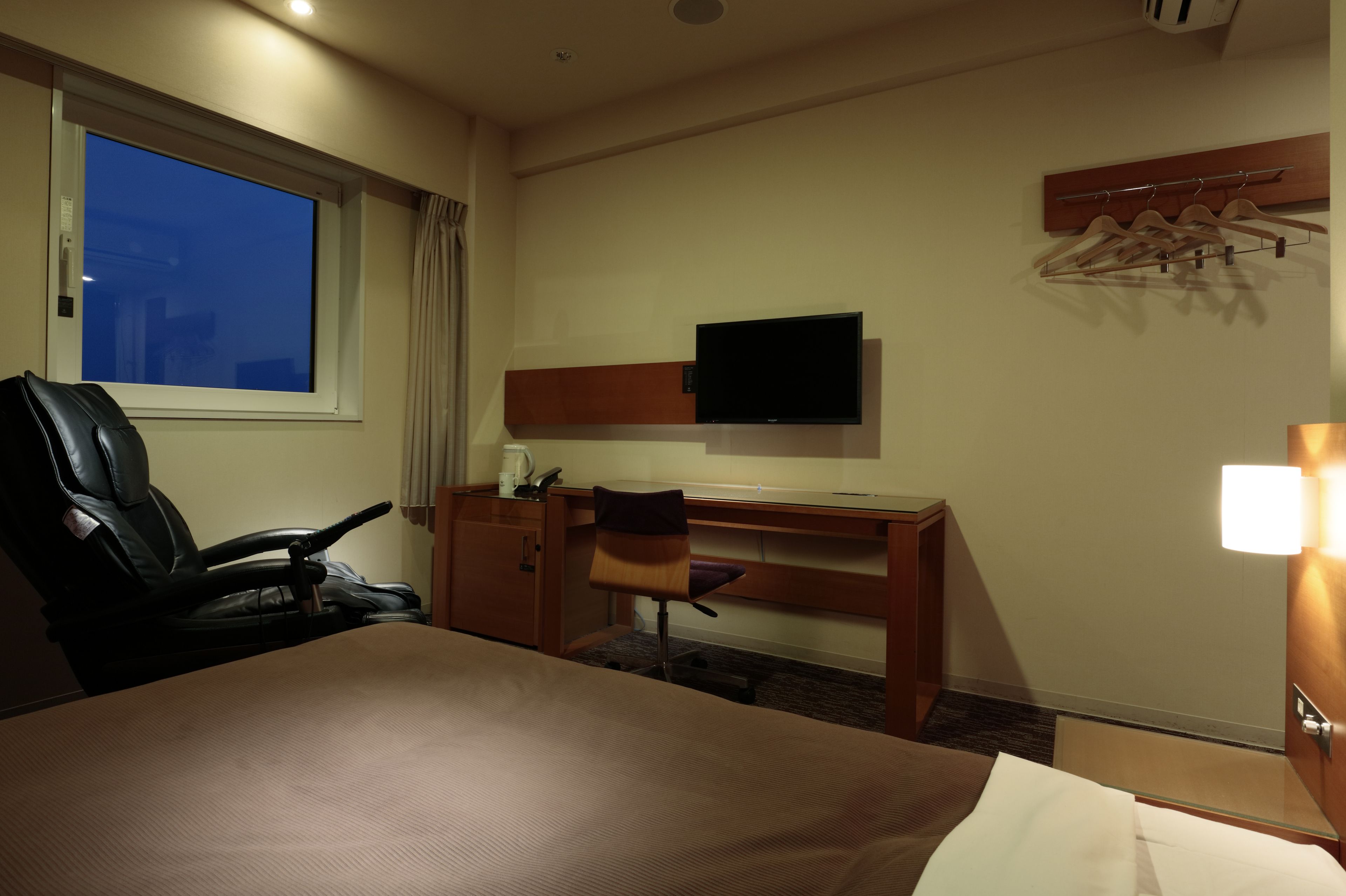 A hotel room with a bed, a desk, a chair, a television, and a window.