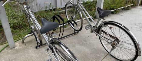 Duas bicicletas estacionadas em uma superfície de concreto perto de um edifício com cerca de metal.