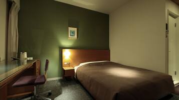 Ein Hotelzimmer mit einem Bett, einem Schreibtisch mit Stuhl, einem Nachttisch mit Lampe und einem gerahmten Bild an der Wand.