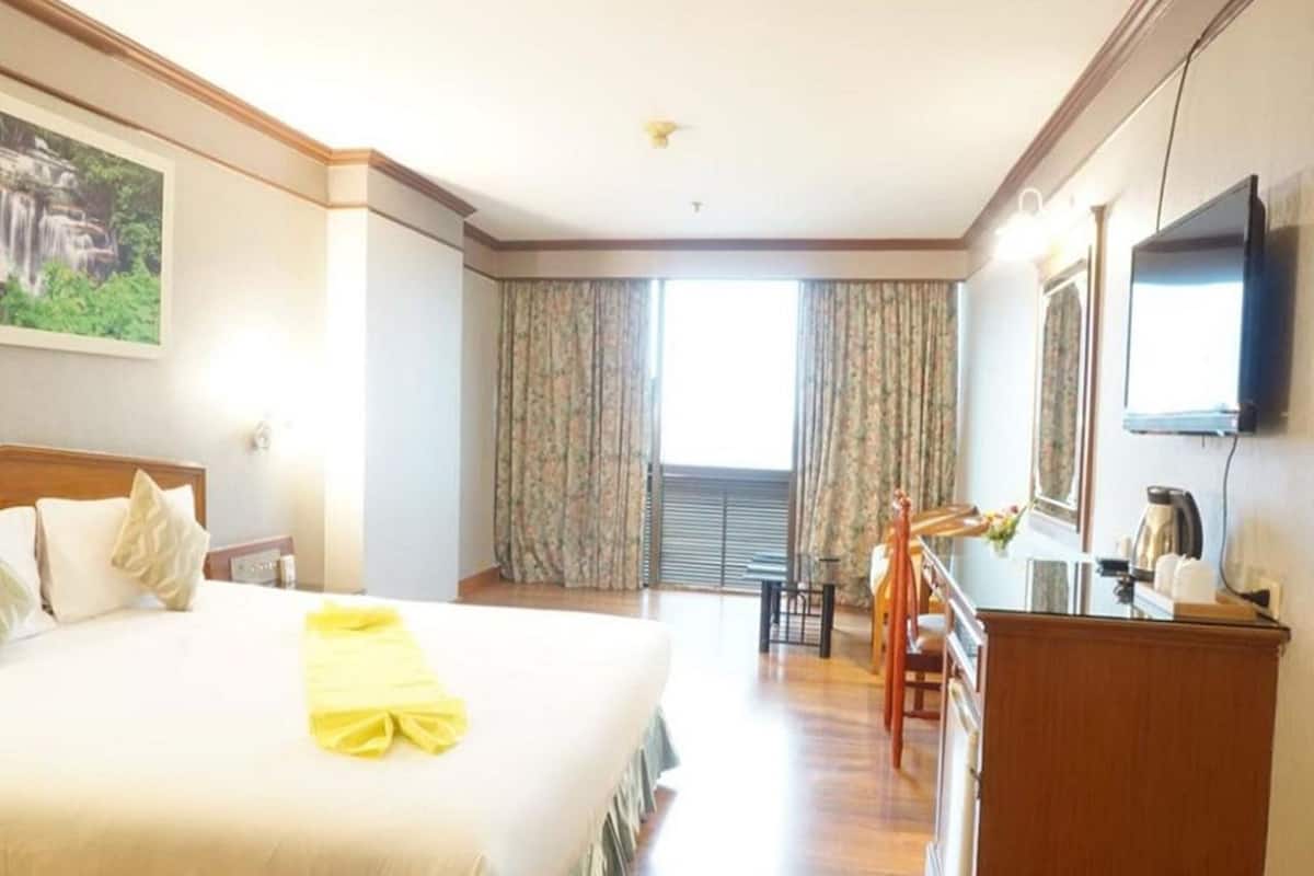A hotel room with a large bed, a desk with a chair, a television, and a window with curtains.