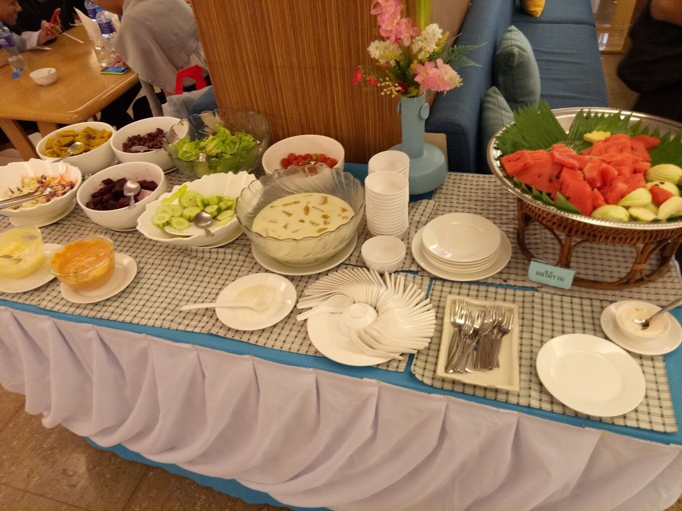 A buffet table with various food items and dishes, including salads, fruits, and a cake.